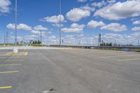 a very large empty parking lot with clouds overhead in the sky in the foreground