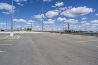 a very large empty parking lot with clouds overhead in the sky in the foreground