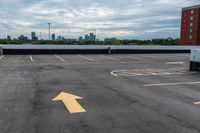 an empty parking lot with buildings in the background and two arrow signs pointing left to right