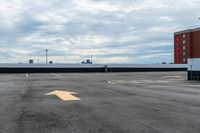 an empty parking lot with buildings in the background and two arrow signs pointing left to right