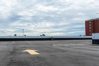 an empty parking lot with buildings in the background and two arrow signs pointing left to right