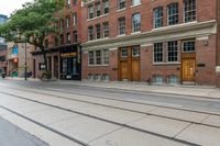 the building on the left has two windows and some doors on the ground in between them and a sidewalk with tracks to each side