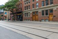 the building on the left has two windows and some doors on the ground in between them and a sidewalk with tracks to each side