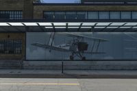 a bus stop on the side of a building next to a parking lot with a plane in it