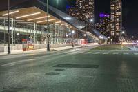 night time image of street at a city intersection with tall buildings behind it and street light traffic passing by