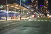 night time image of street at a city intersection with tall buildings behind it and street light traffic passing by