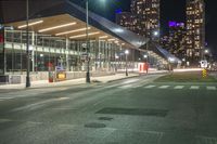 night time image of street at a city intersection with tall buildings behind it and street light traffic passing by