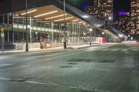 night time image of street at a city intersection with tall buildings behind it and street light traffic passing by