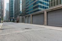 a group of commercial buildings in the city, with some parked cars behind them and some with closed metal doors