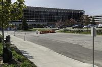 the car park is empty along the road in front of a large building with glass doors