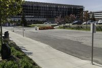 the car park is empty along the road in front of a large building with glass doors