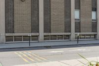 a street with a sign on the sidewalk and a brick building with a bunch of windows