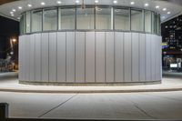 a photo taken at night of the circular building in an empty lot with a bench outside