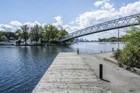 a bridge spanning over the water next to a dock next to trees and water with buildings