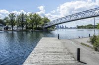 a bridge spanning over the water next to a dock next to trees and water with buildings