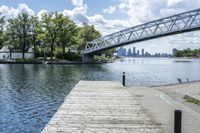 a bridge spanning over the water next to a dock next to trees and water with buildings