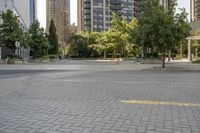 an empty, bricked road with lots of tall buildings and trees on the other side