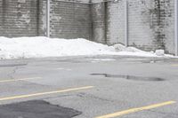 the empty parking lot has only snow on the ground in front of an old brick factory