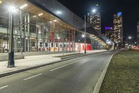 a big glass building next to a street lit up at night time with bright street lights