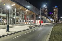 a big glass building next to a street lit up at night time with bright street lights