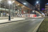 a big glass building next to a street lit up at night time with bright street lights