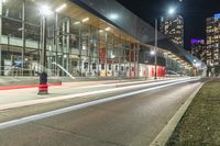 a big glass building next to a street lit up at night time with bright street lights