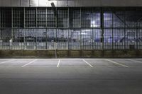 an empty parking lot in front of a building at night with windows and graffiti on the wall