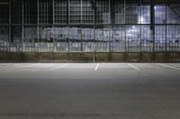 an empty parking lot in front of a building at night with windows and graffiti on the wall