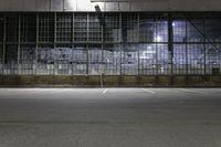 an empty parking lot in front of a building at night with windows and graffiti on the wall