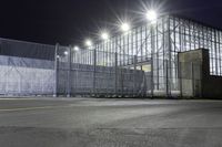 a view of an industrial warehouse from a side walk at night with light on the windows