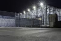 a view of an industrial warehouse from a side walk at night with light on the windows