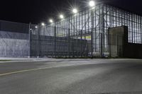 a view of an industrial warehouse from a side walk at night with light on the windows