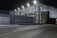 a view of an industrial warehouse from a side walk at night with light on the windows