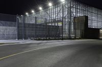 a view of an industrial warehouse from a side walk at night with light on the windows