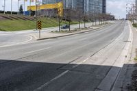 an empty street with cars driving down it and tall buildings in the background across the road