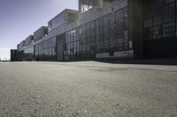 there is a building that looks like a warehouse or factory, near the street and on the right side is a man riding a skateboard