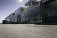 there is a building that looks like a warehouse or factory, near the street and on the right side is a man riding a skateboard