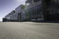 there is a building that looks like a warehouse or factory, near the street and on the right side is a man riding a skateboard