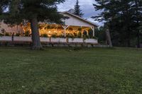 the front porch of a cottage at dusk with fairy lights strung on it's windows