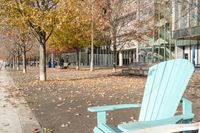 an empty chair on the sidewalk in the fall time, outside of a building on a city block