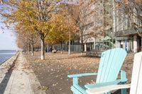 an empty chair on the sidewalk in the fall time, outside of a building on a city block