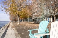 an empty chair on the sidewalk in the fall time, outside of a building on a city block