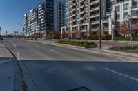 a empty street near tall building in a city setting with the light turned on, and some cars parked on the sidewalk