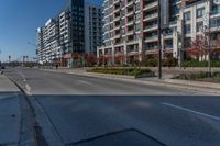 a empty street near tall building in a city setting with the light turned on, and some cars parked on the sidewalk