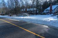 an empty road with a house in the background with lots of snow on it on a sunny day