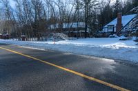 an empty road with a house in the background with lots of snow on it on a sunny day