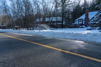 an empty road with a house in the background with lots of snow on it on a sunny day