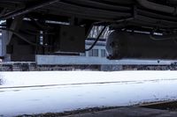 a very long pipe under a building with snow around it and ground covered with icing