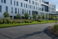 a city street surrounded by grass and tall buildings at the end of a street there is a paved pathway in front of the building