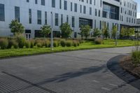 a city street surrounded by grass and tall buildings at the end of a street there is a paved pathway in front of the building